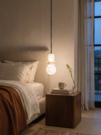 Alabaster Stack Pendant Light hanging low beside a bed over a walnut bedside table in a limewashed bedroom at dusk