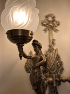 Close-up of a cast brass winged figure lifting a torch with a glowing frosted glass flame shade