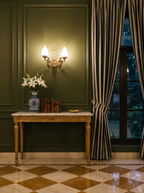 Apsara Double Wall Light glowing above a marble-topped console on a panelled wall in a classical salon at dusk