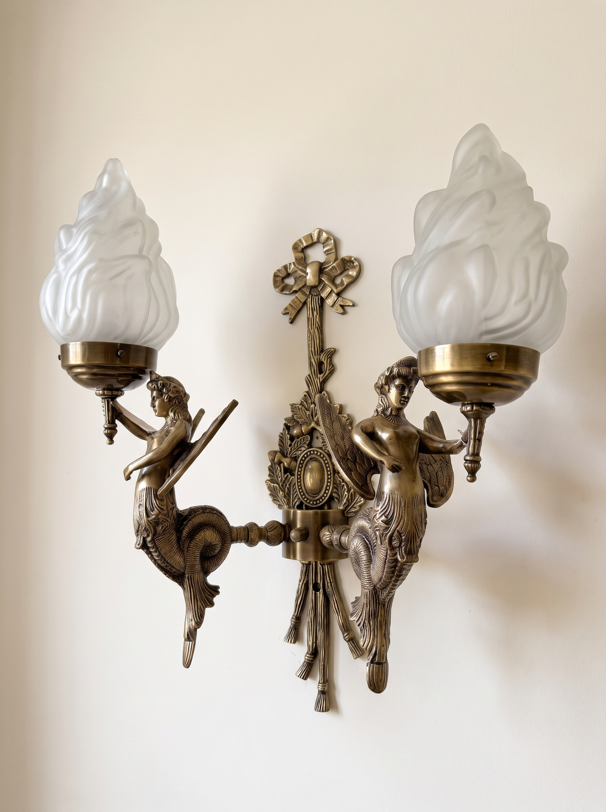 Apsara Double Wall Light three-quarter view, showing the cast winged figures, coiled tails and arms in the round