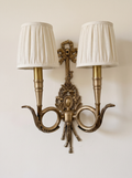 Chasse Cast Brass Double Wall Light, antique brass hunting-horn arms, ribbon bow and oak-leaf trophy with pleated linen shades, front view