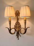 Chasse Double Wall Light switched on, the pleated linen shades glowing warm on the wall