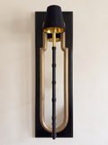 Darpan Mirror Wall Lamp, front view: glossy black panel, gold-framed arched mirror and a black and brass lamp with a black shade