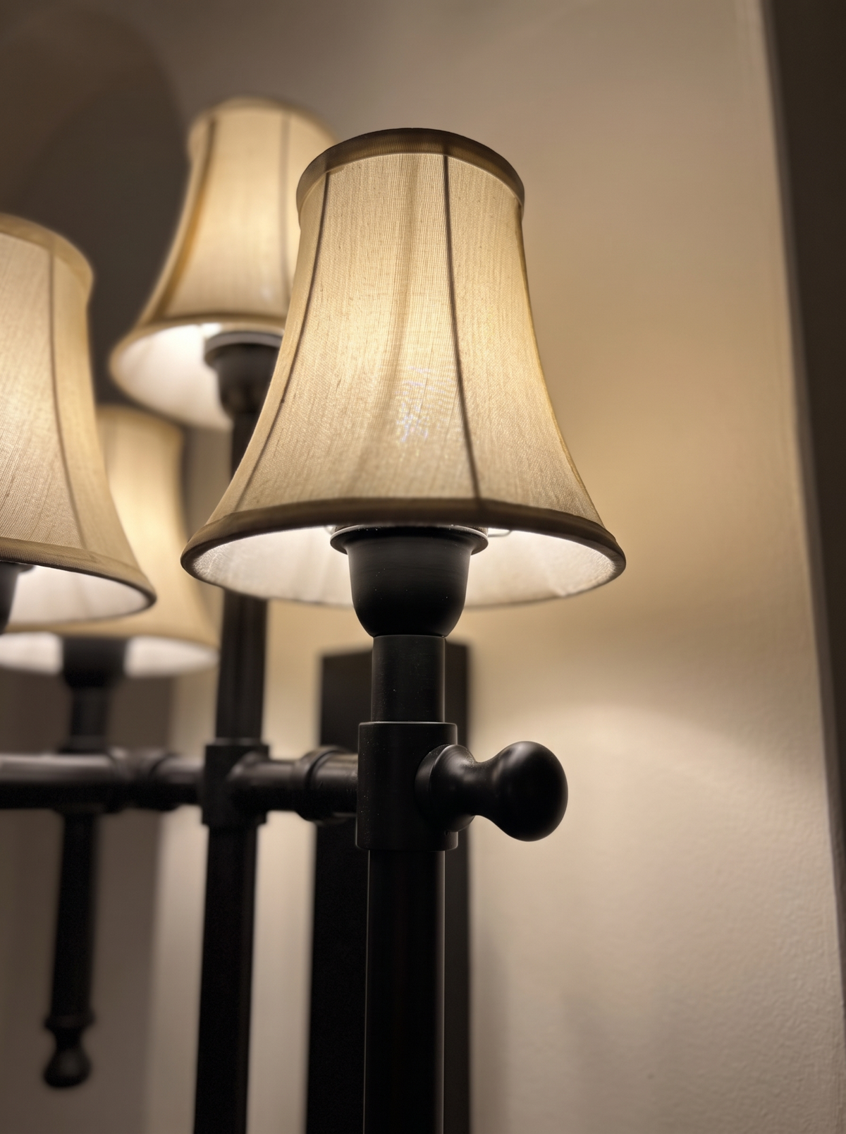 Close-up of a lit off-white fabric bell shade, turned candle cup, collar and ball-knob crossbar in matt black steel