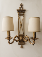 Directoire Brass Double Wall Light, antique brass X-frame backplate with urn finial, two scroll arms and ivory linen shades, front view