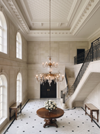 Durbar chandelier lit above a round centre table in a double-height limestone entrance hall with a sweeping staircase
