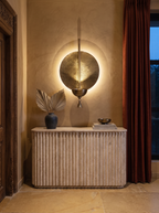 Prabha Halo Wall Light glowing above a fluted travertine console on a textured ochre lime-plaster wall