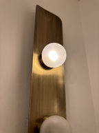 Close-up of a lit frosted glass globe on its brass cup against the brushed, curved antique brass
