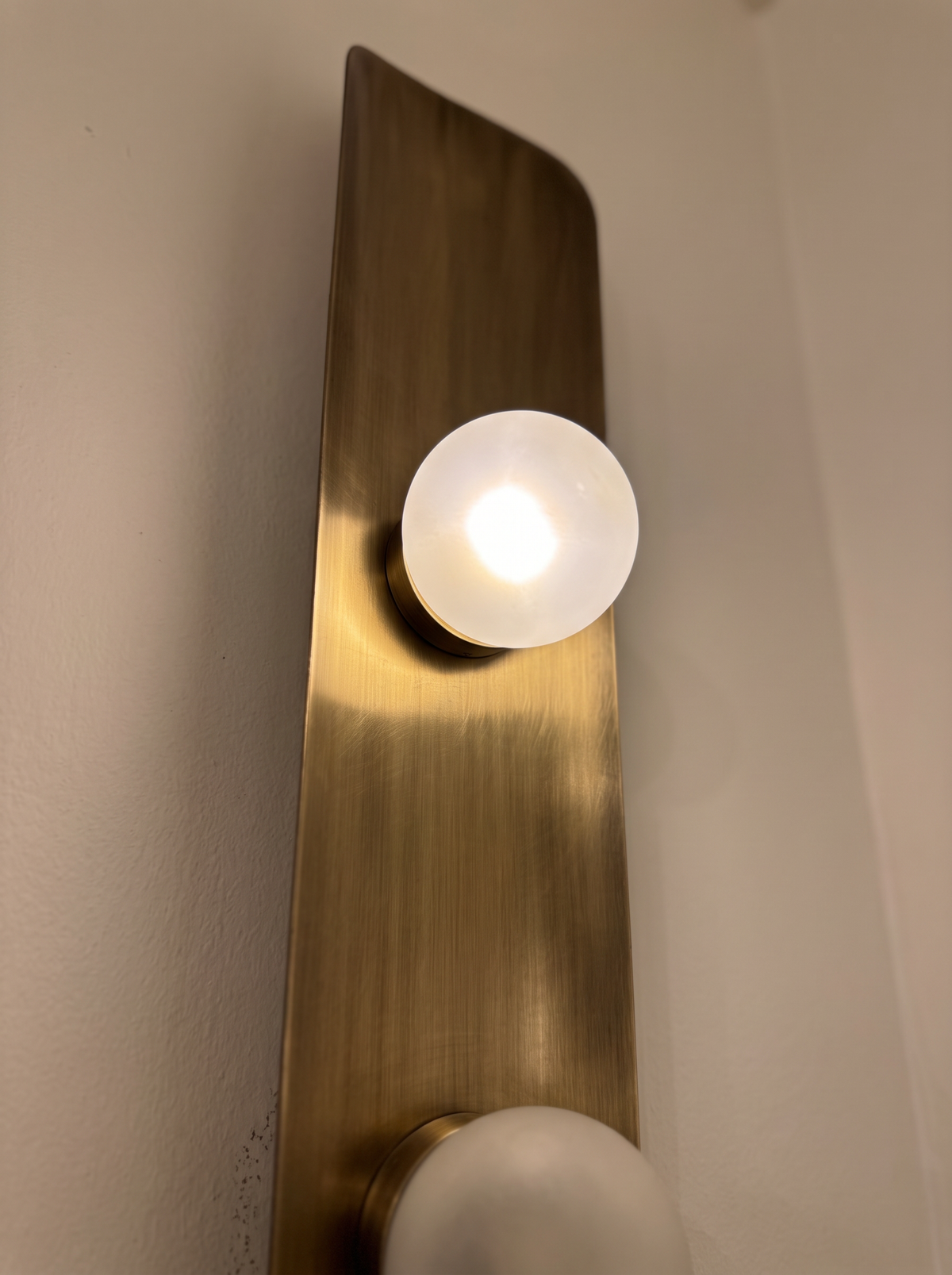 Close-up of a lit frosted glass globe on its brass cup against the brushed, curved antique brass