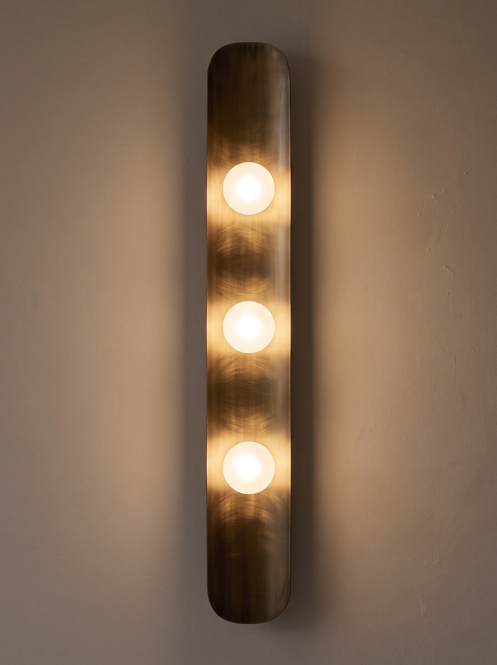 Reed Wall Light switched on, three frosted globes glowing and warm light running down the curved brass