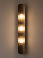 Reed Wall Light switched on, three frosted globes glowing and warm light running down the curved brass